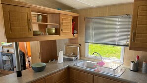 A compact kitchen with wooden cabinets, a built-in microwave, and a window with blinds.