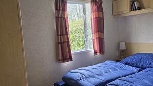 A bedroom with a bed, a window with curtains, a bedside table, and a shelf with books.