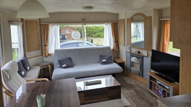 A compact RV interior with a sofa, a coffee table, a TV, and a small dining area.