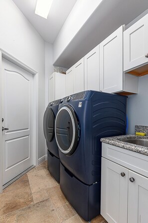 A laundry room with two front-loading washing machines, a sink, and white cabinetry.