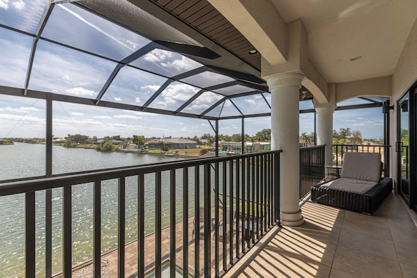 A balcony with a view of a body of water, a chair, and a table.