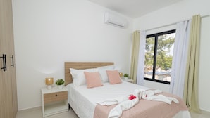 Une chambre à coucher comprenant un lit, des tables de chevet, un climatiseur et une fenêtre avec des rideaux.