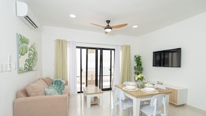 Un salon moderne comprenant un canapé, une table à manger, des chaises, un ventilateur de plafond et un téléviseur fixé au mur.