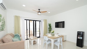 Un salon moderne comprenant un canapé, une table à manger avec des chaises, un ventilateur de plafond, un téléviseur et un distributeur d’eau.