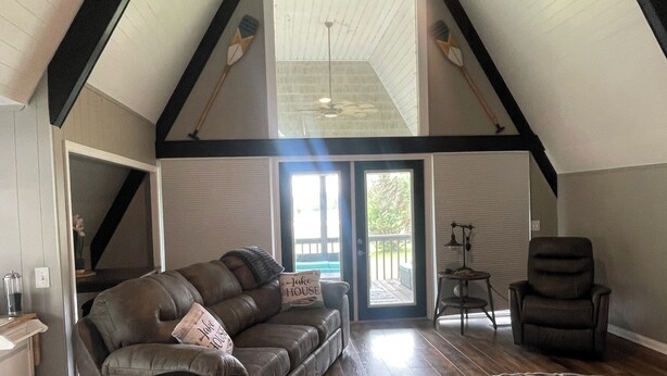 Geräumiges Loft mit hohen Decken, einem Deckenventilator, einem großen Fenster, einem braunen Ledersofa, einem gemusterten Teppich und Holzboden.