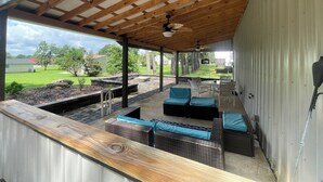 Ein überdachter Patio-Bereich mit Außenmöbeln, einem Deckenventilator und Blick auf eine grüne Landschaft.