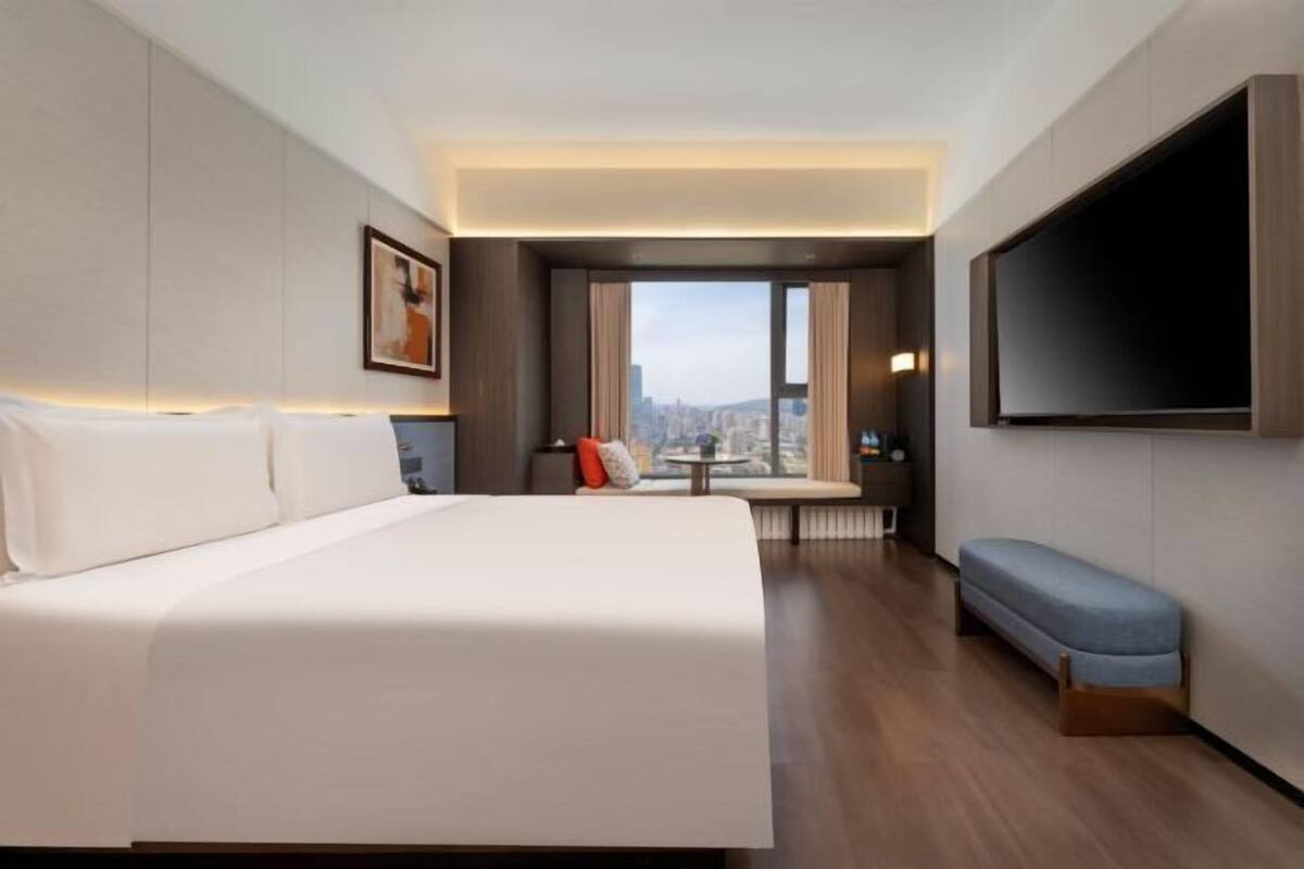 Una camera d'hotel con un letto grande, una panca, un televisore e vista sulla città.