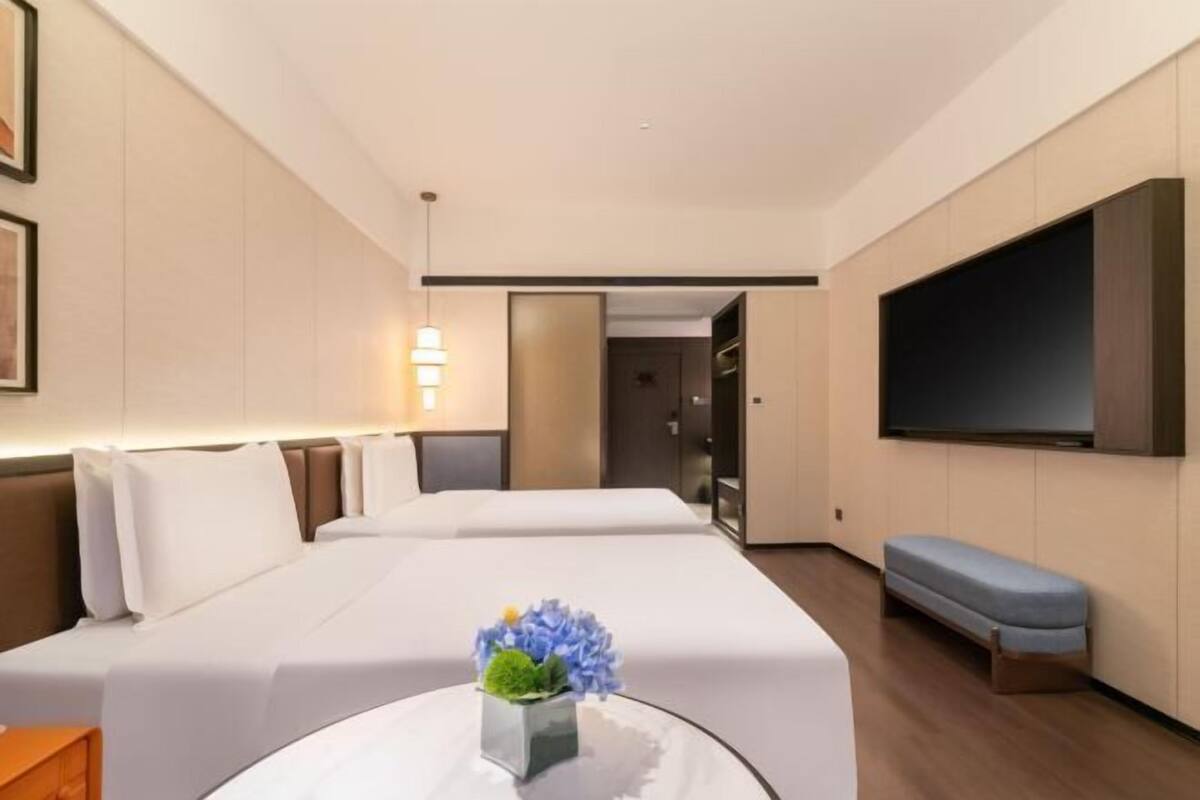 Una camera d'albergo con due letti, una TV a schermo piatto, un comodino e una piccola zona salotto.