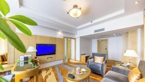 A modern hotel room with a flat-screen TV, a sofa, a coffee table, and a desk with a lamp. - JJ Sun Hotel (Lanzhou)