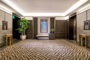Un hall d’hôtel avec un tapis à motifs, une grande plante en pot, un banc et des œuvres d’art encadrées accrochées aux murs.
