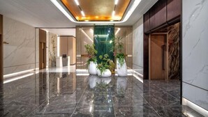 Um hall de hotel moderno com piso de mármore polido, um arranjo de plantas central e um elevador de madeira.