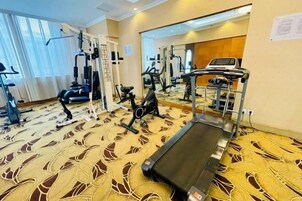 Academia de hotel com equipamentos de cardio, máquinas de peso e um espelho grande.