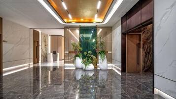 A hotel lobby with a polished marble floor, a central plant arrangement, and a modern ceiling design.