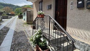 Calle adoquinada de piedra que lleva a un edificio con puerta de madera y balcón con plantas en macetas.