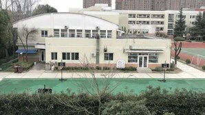 A multi-story building with a flat roof, a basketball court, and a green field in front. - Jinlu Business Hotel (Shanghai)