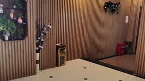 A hotel lobby with a tiled floor, a wooden panel wall, a small plant display, and a red trash bin. - Jinlu Business Hotel (Shanghai)