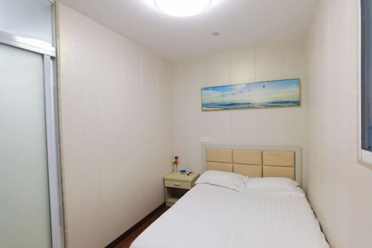 Quarto com cama, mesa de cabeceira, quadro e janela.