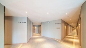 Un long couloir étroit, typique d’un hôtel, avec des murs de couleur claire et un plancher en bois.
