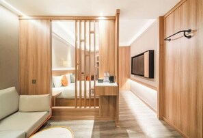 A modern, compact room with a wooden partition, a sofa, a small table, and a TV mounted on the wall. - YanxI Hotel (Shanghai)