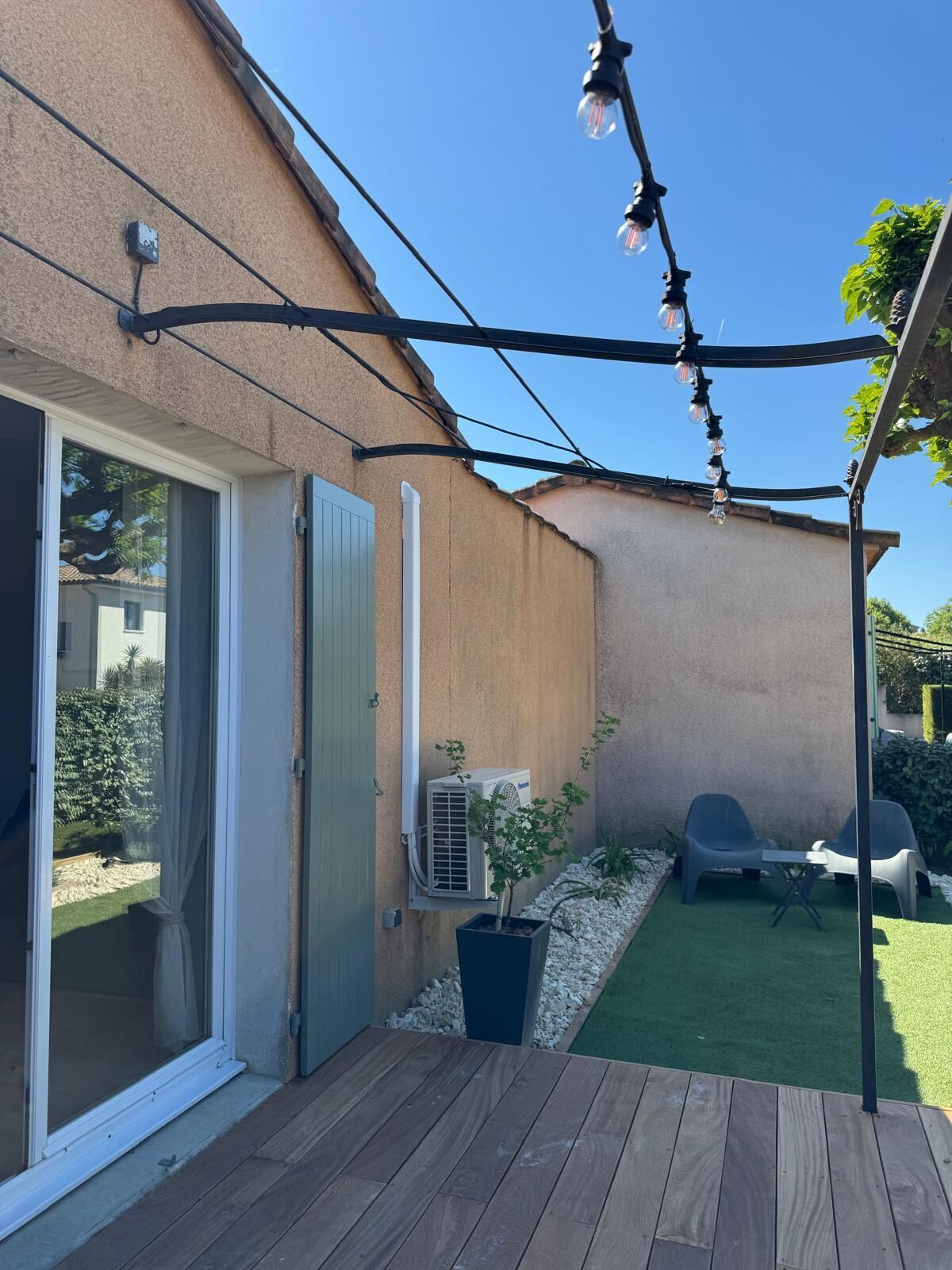 Eine Holzterrasse mit einer Schiebetür, eine kleine Terrasse mit Tisch und Stühlen und eine Lichterkette.