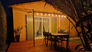 Une terrasse en bois avec une table et des chaises, une porte-fenêtre coulissante et des guirlandes lumineuses.