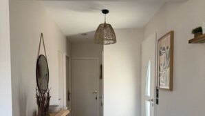 Un couloir doté d’un plancher en bois, d’une suspension lumineuse, d’un miroir et d’une œuvre d’art encadrée accrochée au mur.