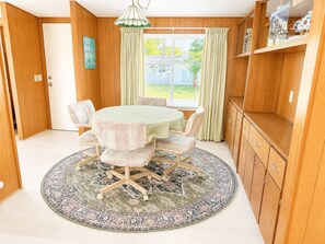 A dining room with a round table, chairs, a patterned rug, wooden cabinets, and a view through the window.