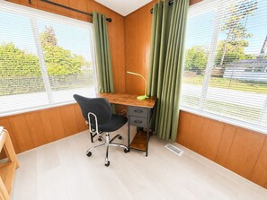 Um quarto com uma escrivaninha de madeira, uma cadeira de escritório preta e uma janela com cortinas verdes.