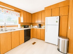 A kitchen with wooden cabinets, a white refrigerator, a dishwasher, a sink, and a trash can.