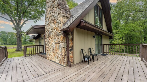 A wooden deck with chairs, a stone pillar, and a building with a sloped roof. - Rustic charm with modern amenities, ensuring a comfortable and memorable stay. (Mountain View)