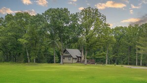 A house surrounded by a large grassy field and dense trees. - Rustic charm with modern amenities, ensuring a comfortable and memorable stay. (Mountain View)