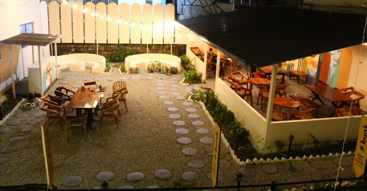 Un'area patio esterna con un angolo salotto, un muro bianco curvo e un piccolo giardino.