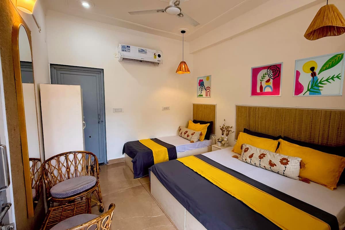 A hotel room with two beds, a ceiling fan, an air conditioner, and a chair.
