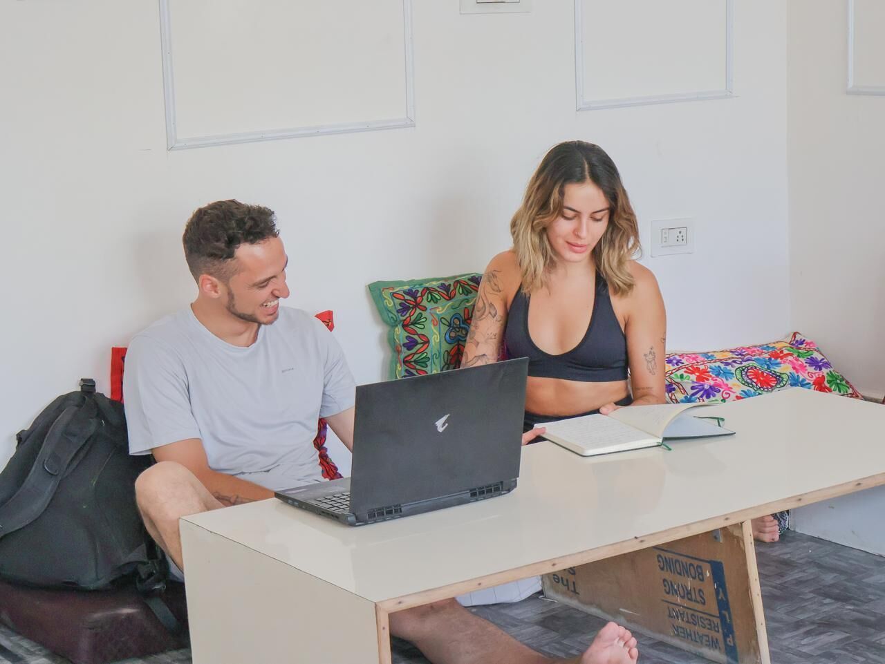 Two people sitting at a table with a laptop and a notebook.
