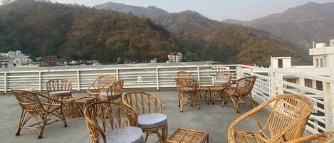 A rooftop terrace with wicker furniture and a view of a mountainous landscape.