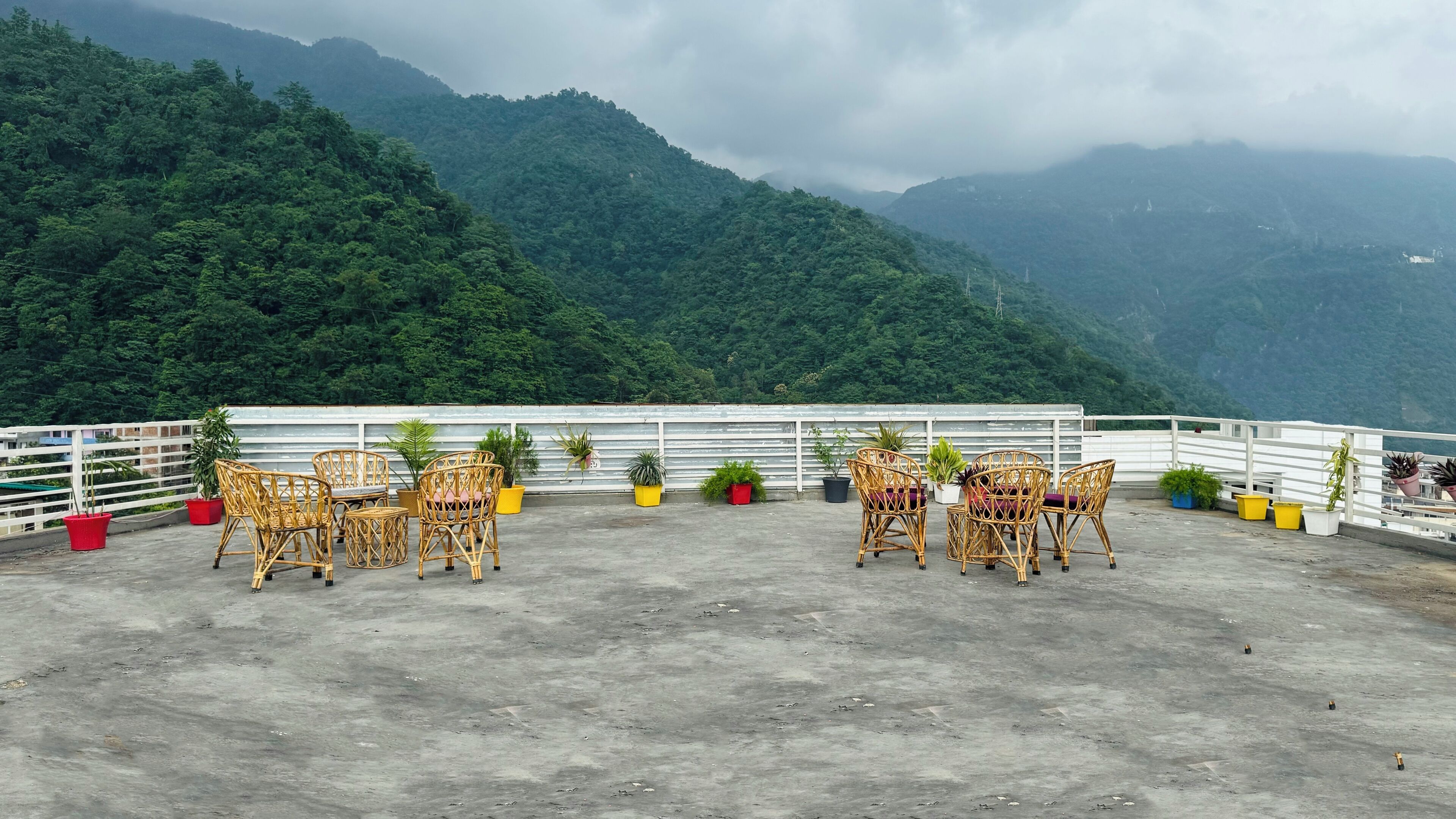 Une terrasse sur le toit, aménagée avec des meubles en osier et des plantes en pot, offrant une vue sur un paysage montagneux.