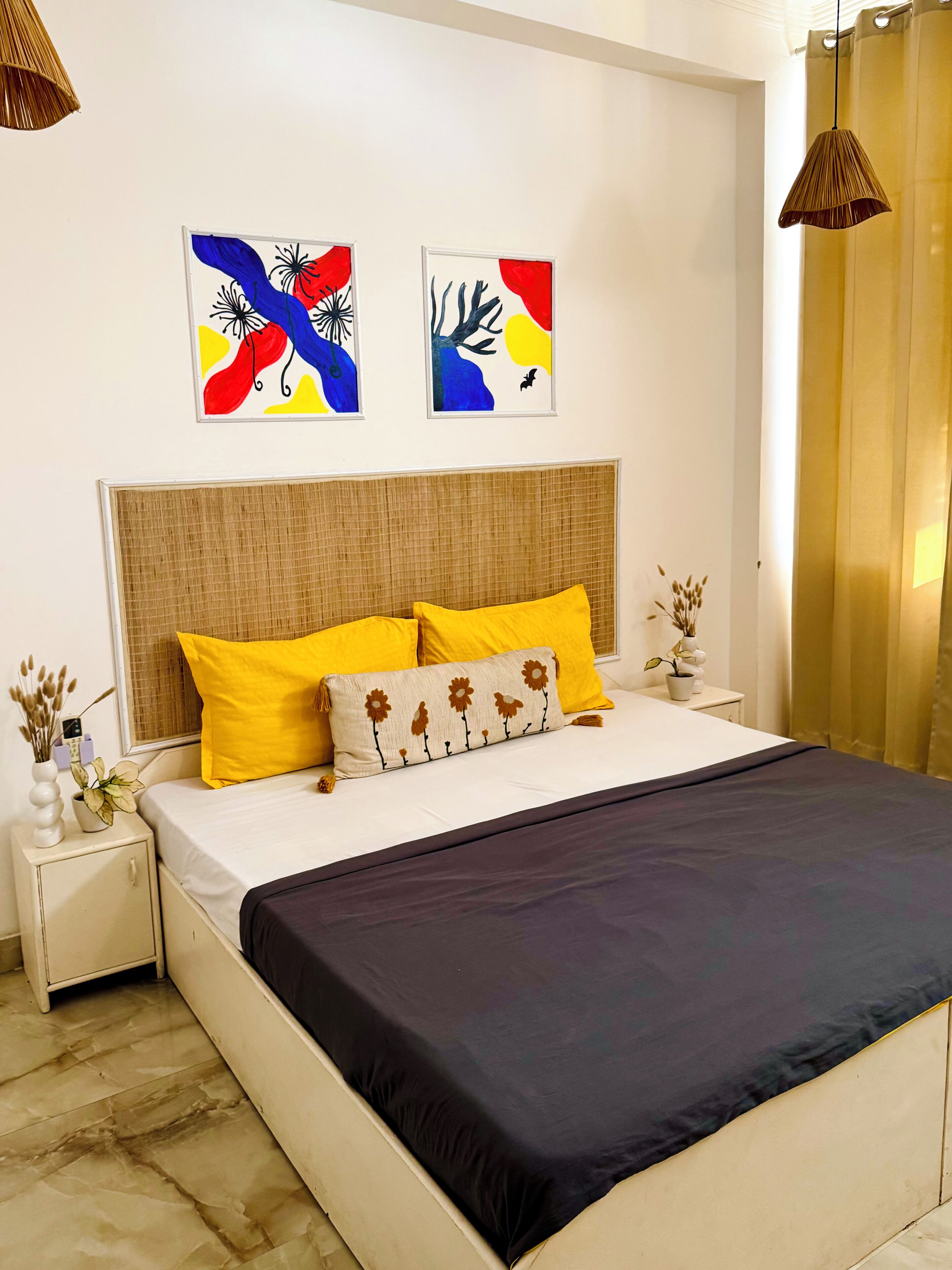 Une chambre à coucher comprenant un lit, deux tables de chevet, une tête de lit et deux tableaux abstraits accrochés au mur.