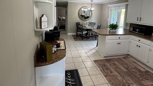 A modern kitchen with white cabinetry, a dining area with a round table, and a coffee bar with a sign.
