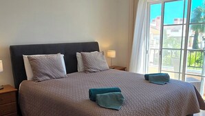 A bedroom with a large bed, two bedside tables, and a window with curtains. - Charming 2-bedroom in a luxury enclosed condominium in Vila Sol with AC, WiFi (Quarteira)
