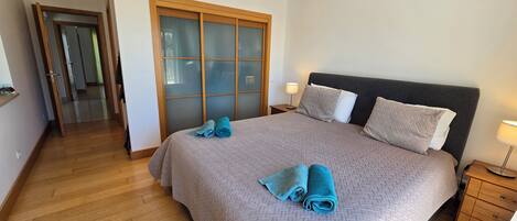 A bedroom with a bed, two nightstands, a wooden wardrobe, and a door leading to another room.