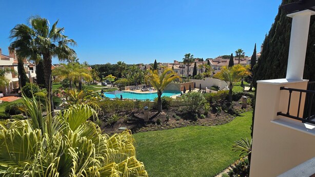 A pool area with a clear blue pool, surrounded by palm trees and a well-maintained lawn. - Charming 2-bedroom in a luxury enclosed condominium in Vila Sol with AC, WiFi (Quarteira)