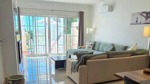 A spacious living area with a large sofa, a dining table, and a view through glass doors to an outdoor patio. - Charming 2-bedroom in a luxury enclosed condominium in Vila Sol with AC, WiFi (Quarteira)