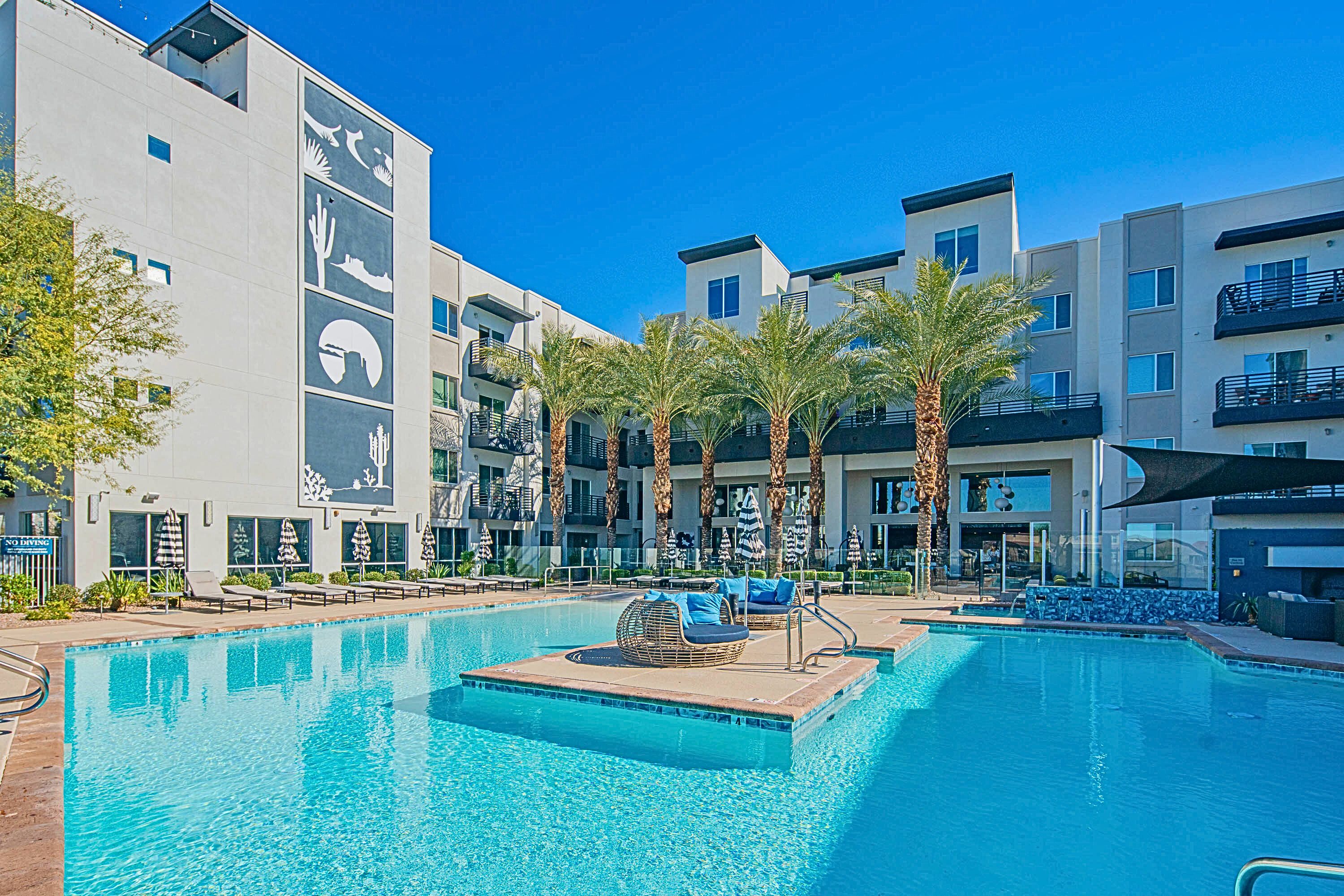 A modern hotel with a swimming pool, palm trees, and lounge chairs.