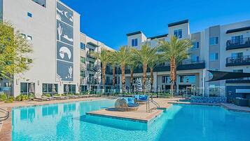 A modern hotel with a swimming pool, palm trees, and lounge chairs.