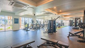 A spacious gym with various exercise equipment, large windows, and a view of the outdoors.