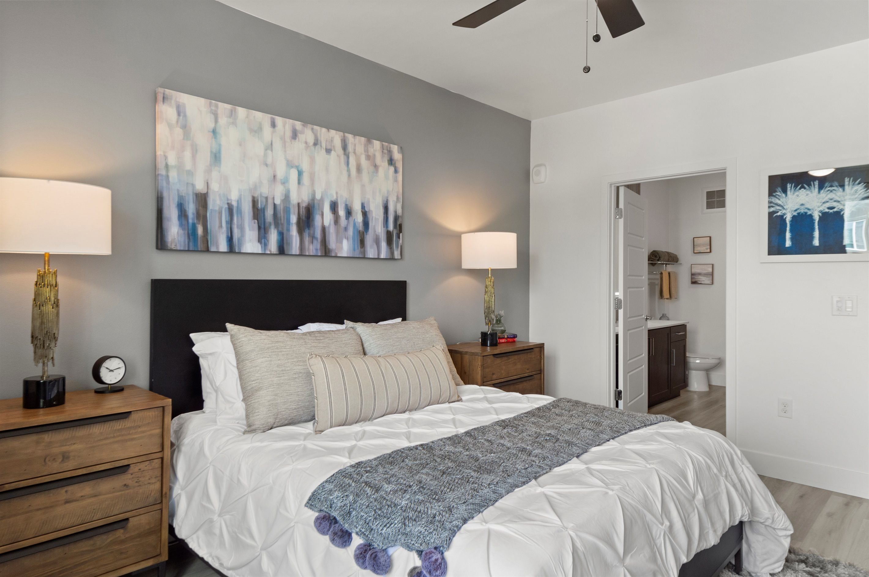 A bedroom with a bed, two bedside tables, a nightstand, a ceiling fan, and a painting on the wall.