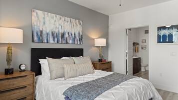 A bedroom with a bed, two bedside tables, a nightstand, a ceiling fan, and a painting on the wall.