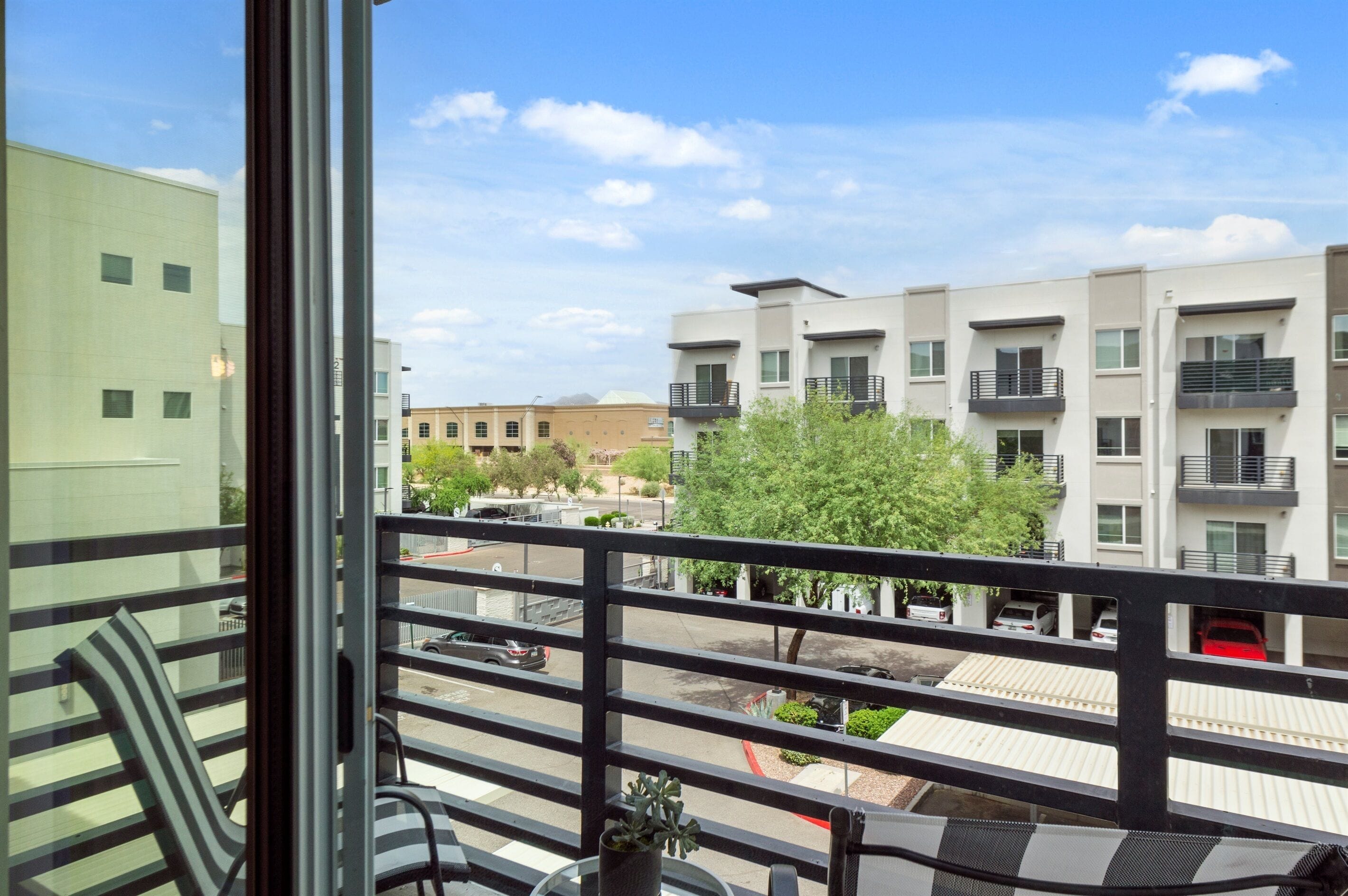 A balcony with a view of modern buildings, a parking area, and a clear sky.