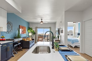 Apartamento moderno con cocina, sala de estar y dormitorio. Cuenta con un ventanal grande, ventilador de techo y vistas de la ciudad.