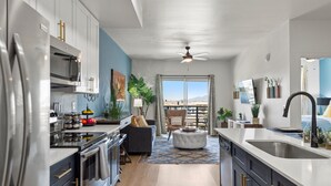 A modern kitchen with a central island, a dining area with a sofa, and a view of a mountainous landscape through a large window. - Kierland Area | Sun-Kissed Stay | Pool & Hot Tub (Phoenix)